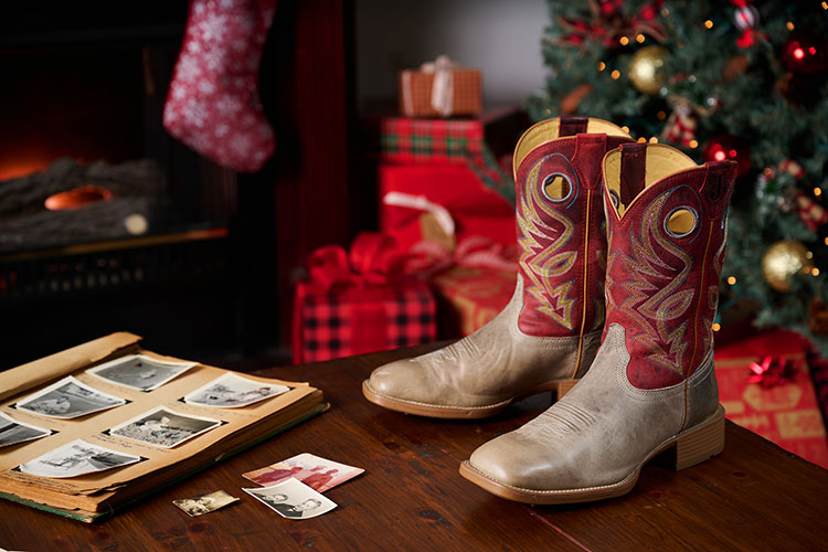 Zapato Pickett de 11” de punta cuadrada ancha para hombre en color gris colocado sobre una mesa con un fondo navideño detrás.